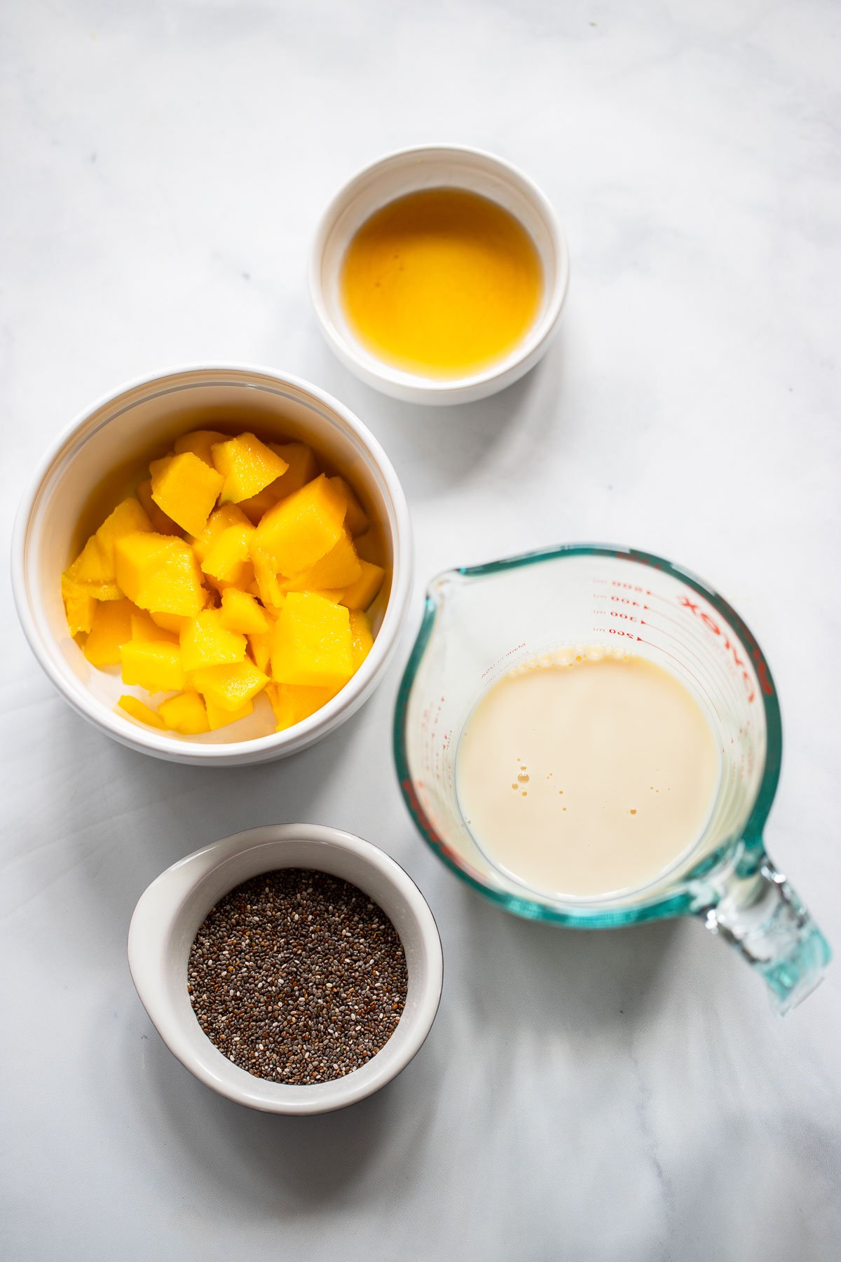 Mango chia seed pudding ingredients in small plates on white background.