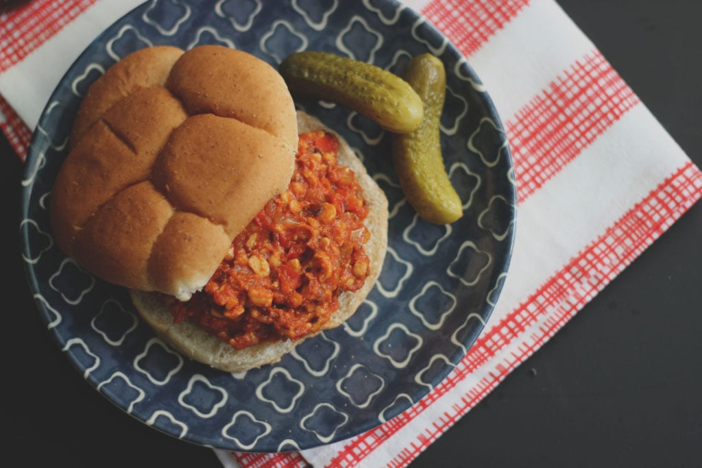 Vegan Sloppy Joe sandwich on a blue plate with a pickle on the side. 