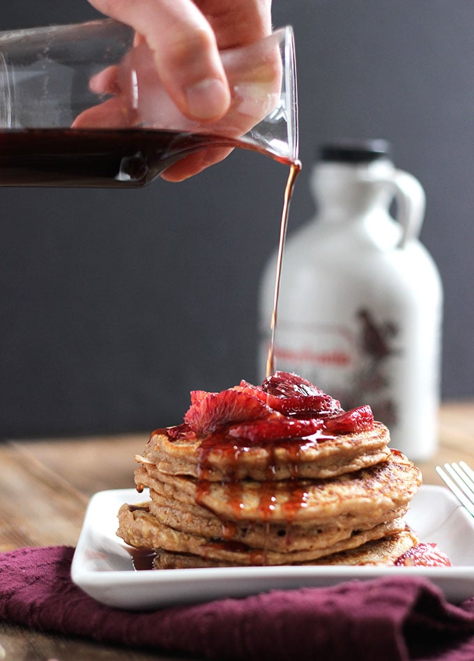 Blood Orange Buttermilk Pancakes with hand pouring maple syrup onto the stack. 