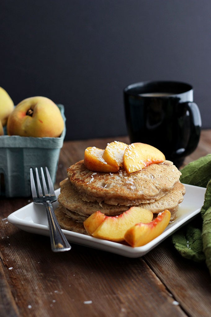 Vegan Oatmeal Pecan Pancakes topped with sliced peaches on a square plate. 