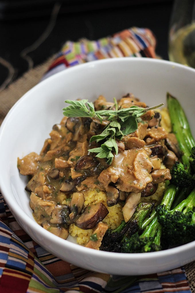 Vegan Seitan and Mushrooms with Polenta with broccoli in a white bowl.