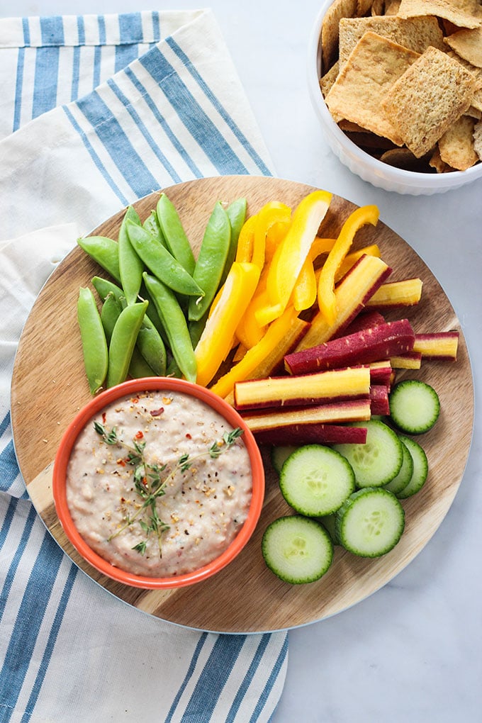Lemon Herb White Bean Dip in a small bowl on a board with cut vegetables. 