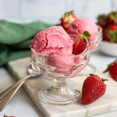 vegan strawberry frozen yogurt in a glass ice cream dish with a fresh strawberry for garnish.