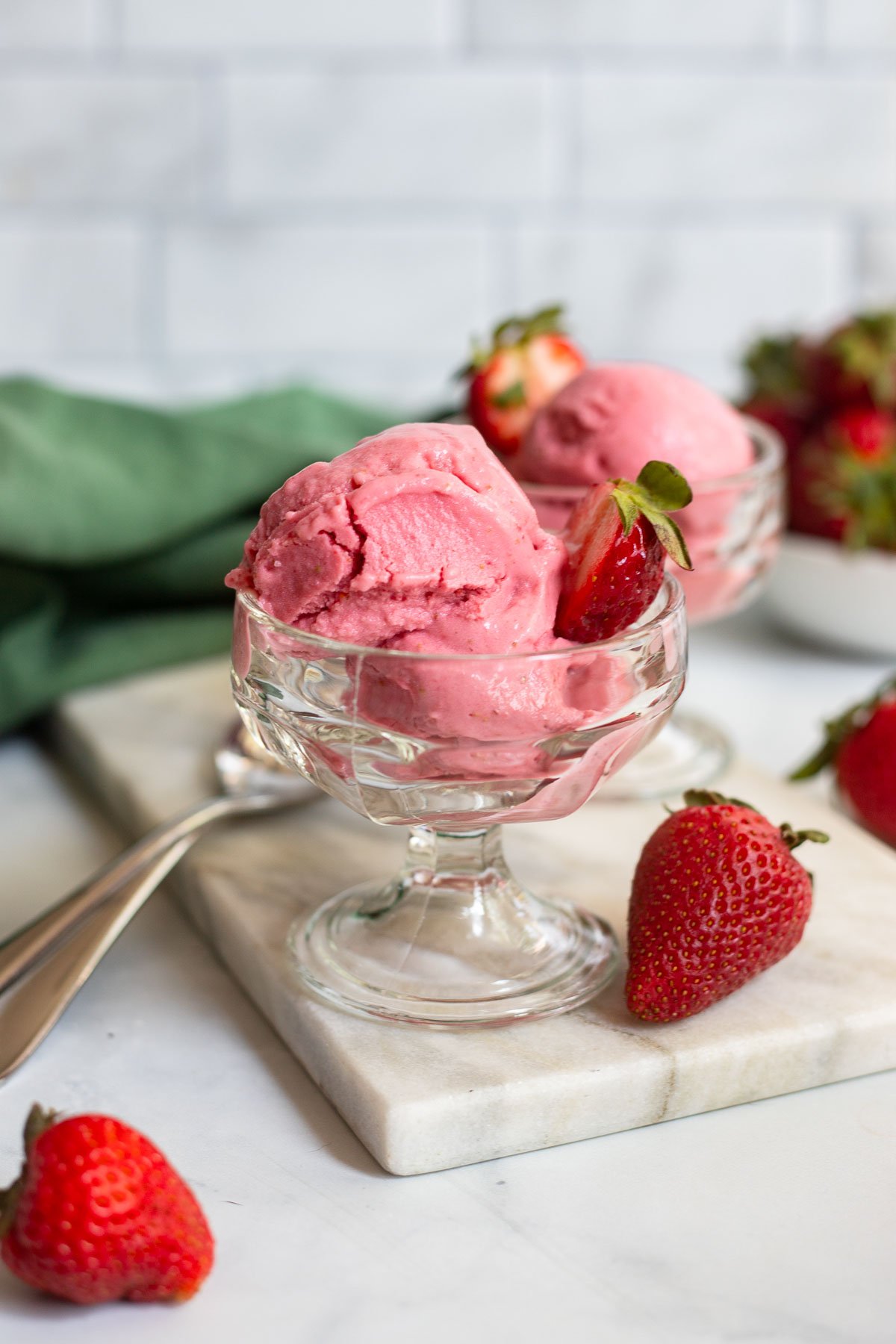 vegan strawberry frozen yogurt in a glass ice cream dish with a fresh strawberry for garnish.