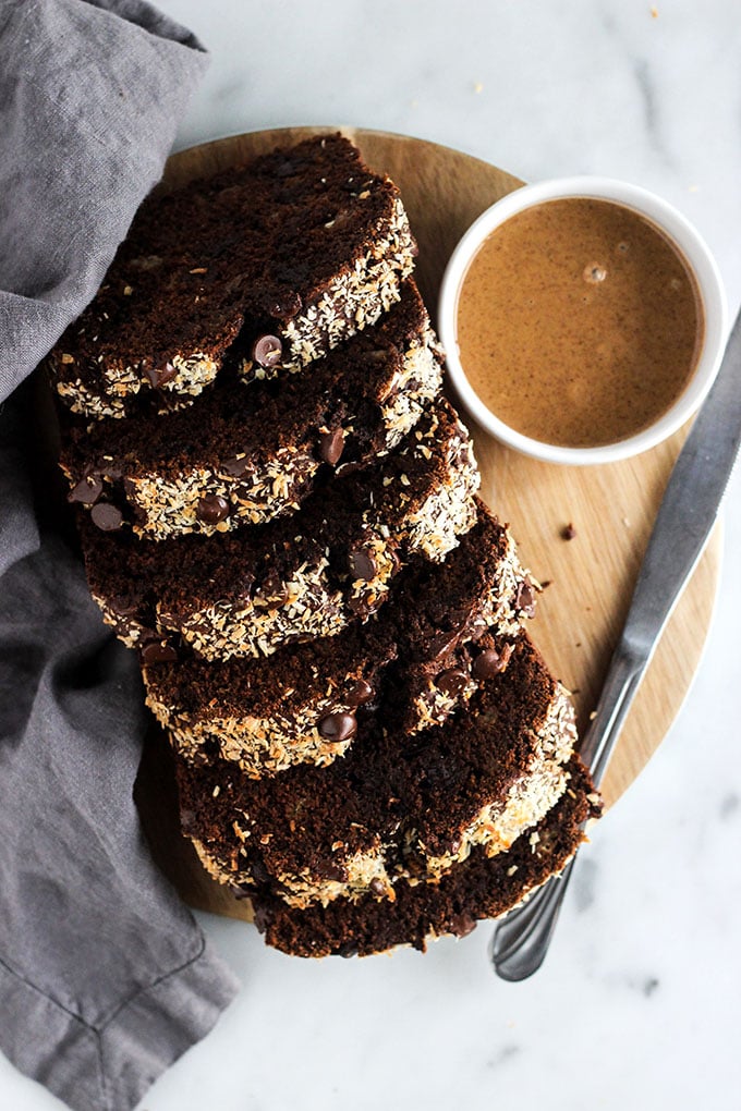 sliced mocha banana bread on a round cutting board with a dish of peanut butter.