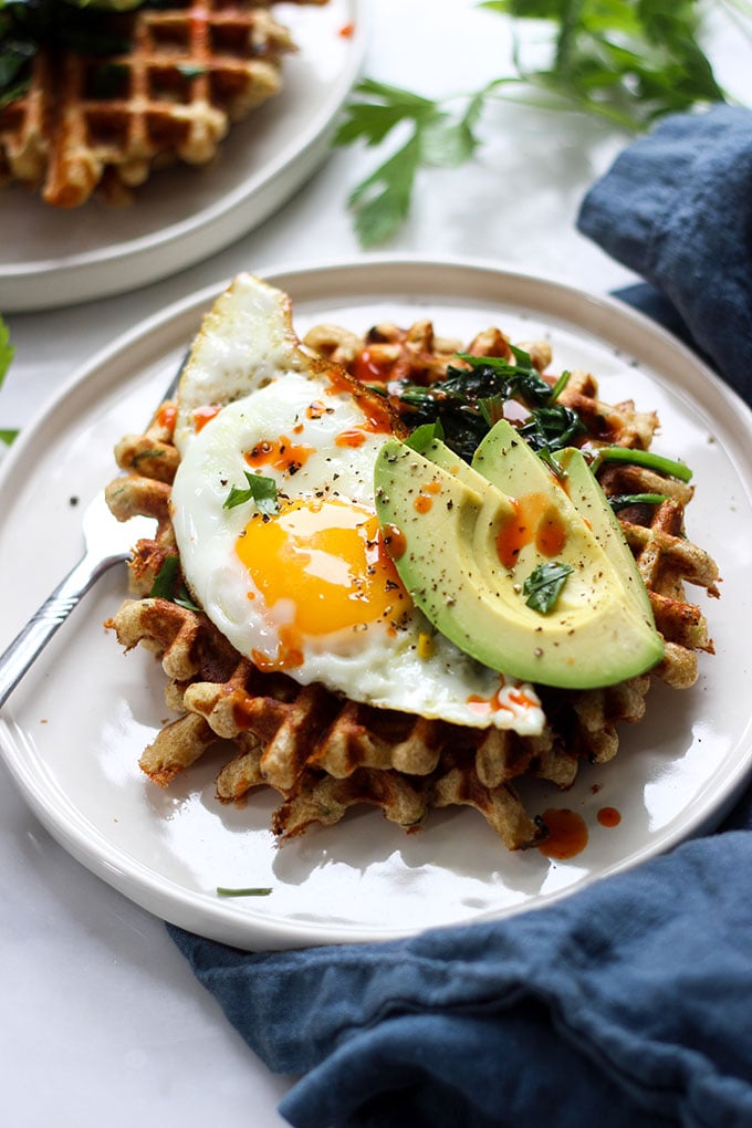 Savory Cheddar Zucchini Waffles topped with a fried egg on a white plate. 