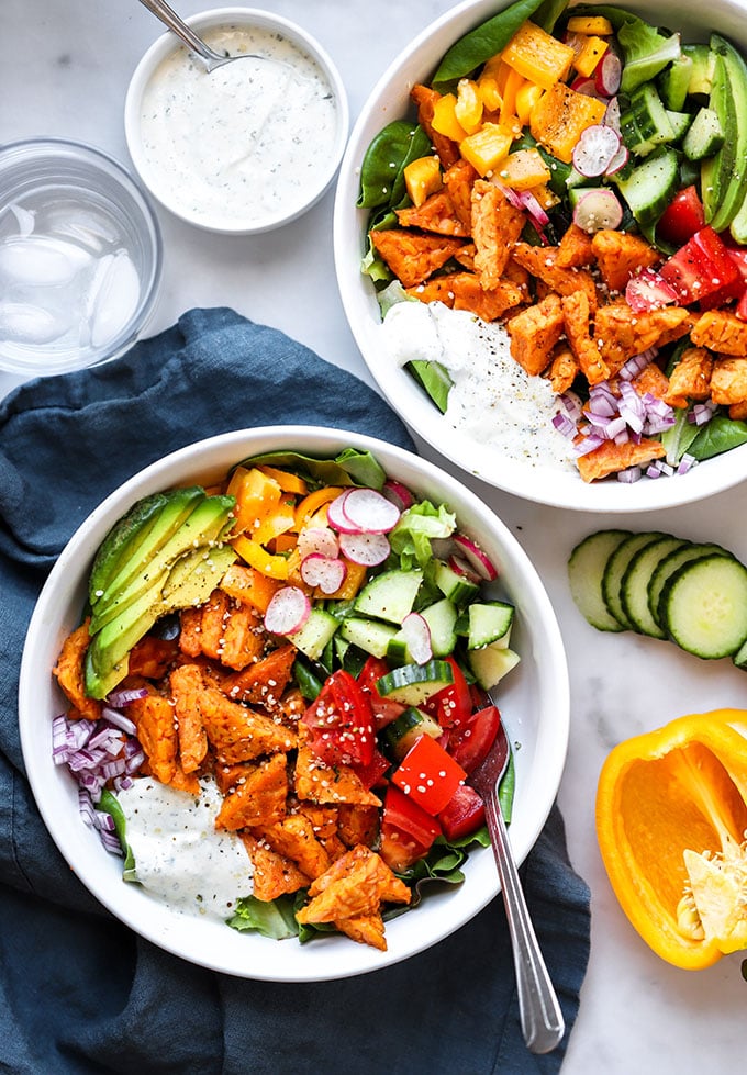 colorful buffalo tempeh salad in white bowl with fork.