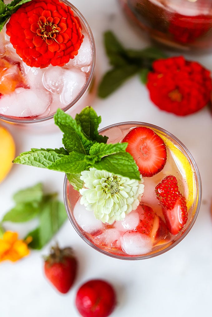 strawberry peach sangria in a glass garnished fresh mint and a flower.