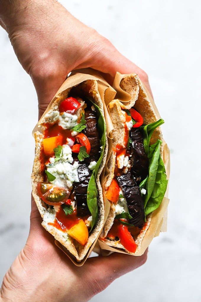 hands holding a sliced Roasted Eggplant and Pepper Pita Sandwich.