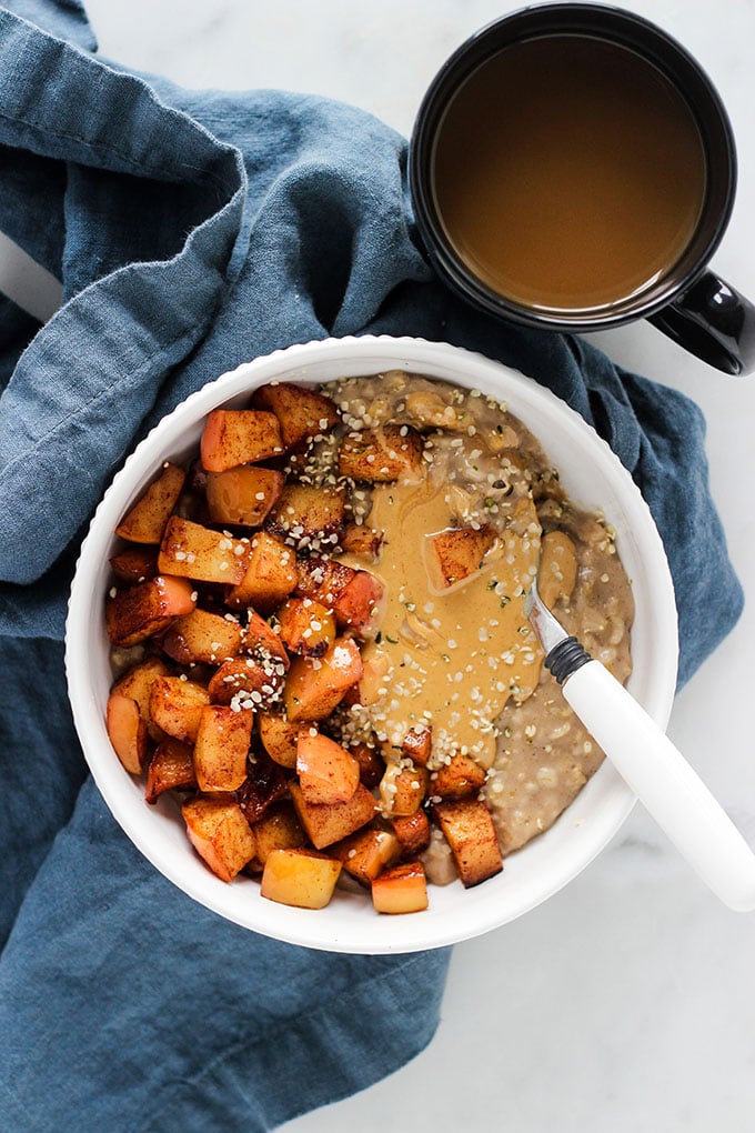 Oatmeal with sautéed cinnamon apples and peanut butter in white bowl with blue napkin