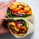 Tempeh wrap with peanut sauce held up with hand