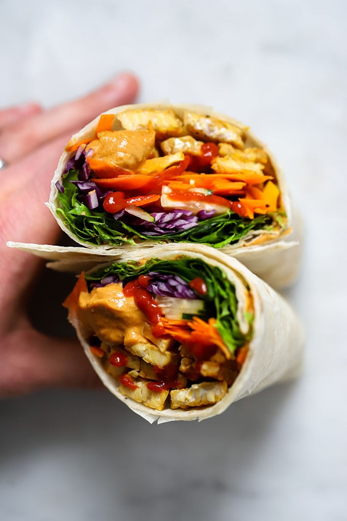 Tempeh wrap with peanut sauce and colorful vegetables with hand