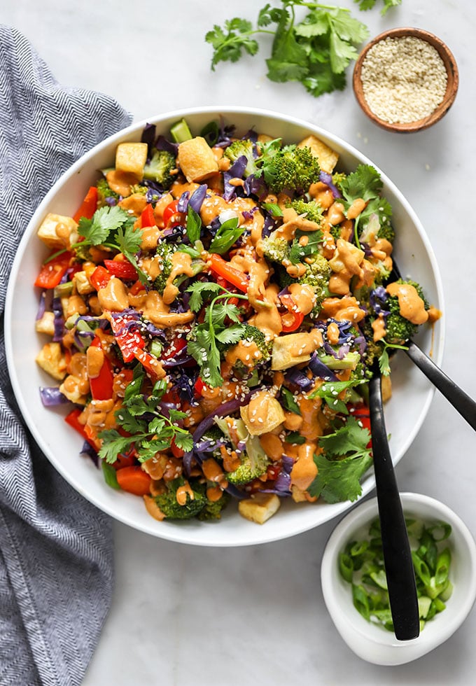 Tofu Stir Fry with Peanut Sauce and Mixed Vegetables in a white bowl with serving spoons. 