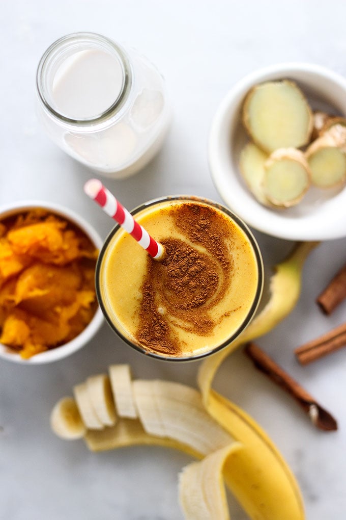 pumpkin smoothie in glass with straw and swirled cinnamon on top.