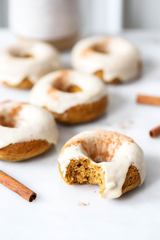 vegan baked pumpkin donuts with maple frosting on white marble background.