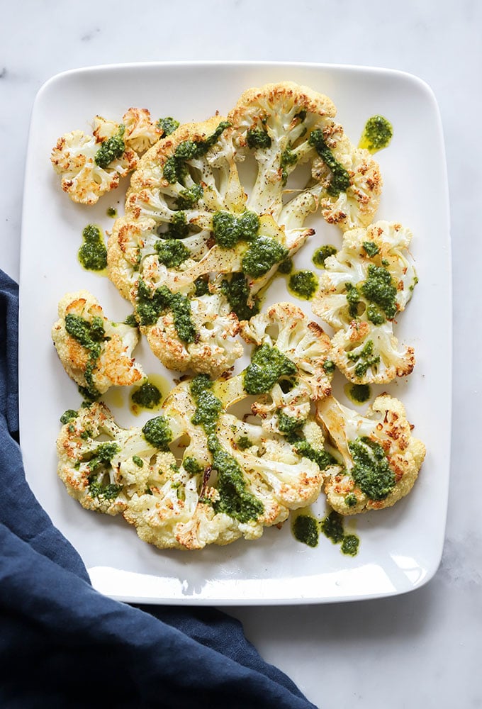 cauliflower steaks drizzled with pesto on a serving dish.