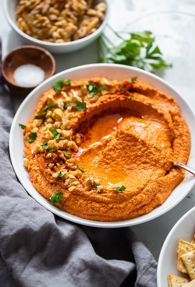 vegan roasted red pepper dip in bowl garnished with chopped walnuts and parsley.