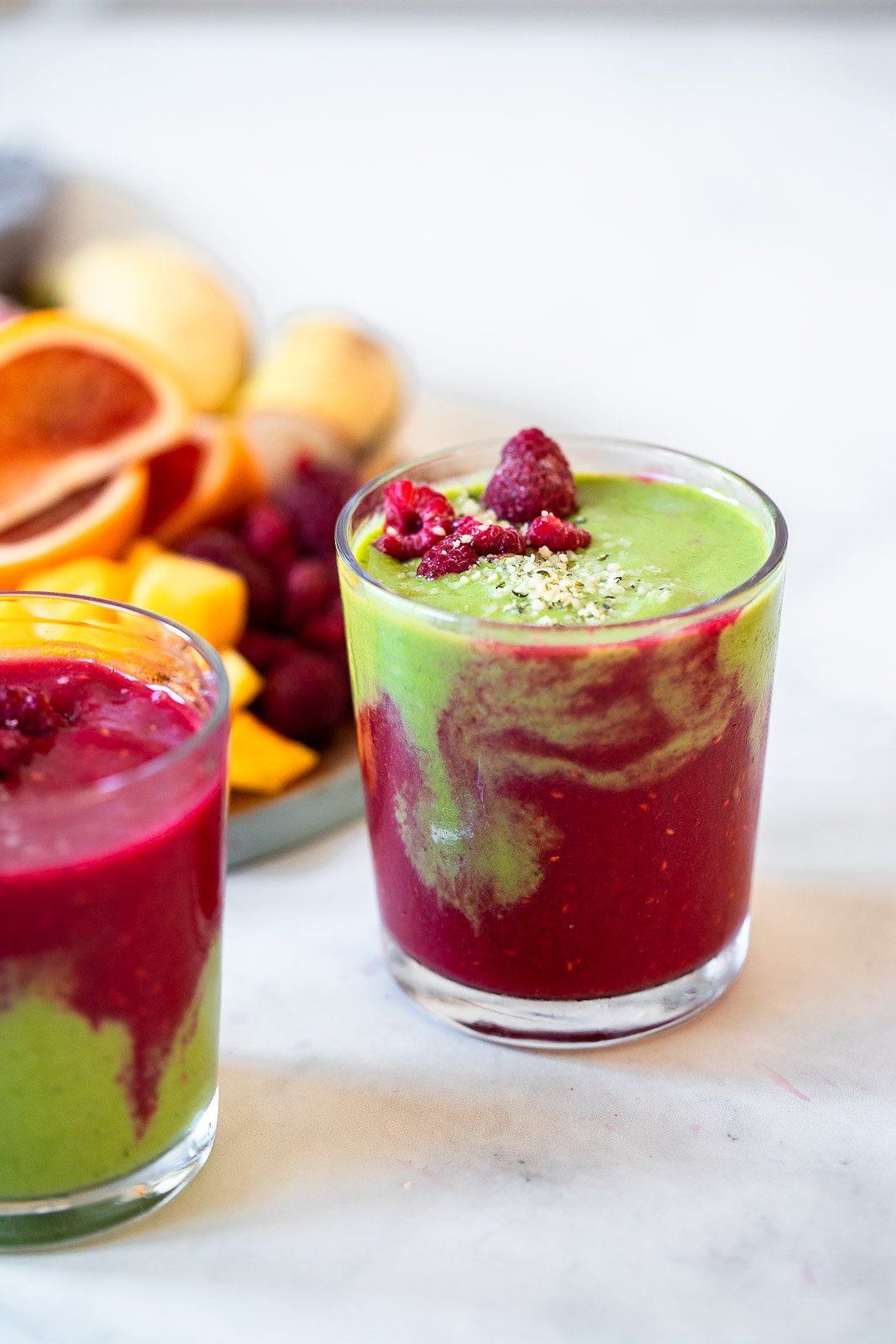 red and green layered smoothie in glass with fresh fruit.