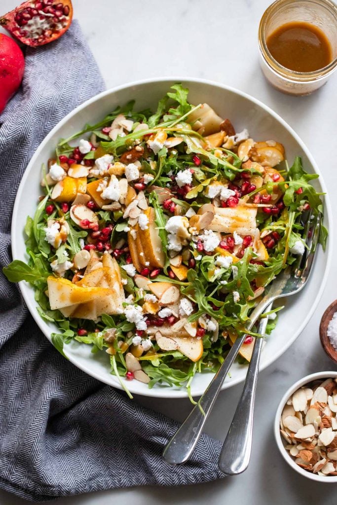 pear salad with pomegranate and balsamic dressing in large white bowl.