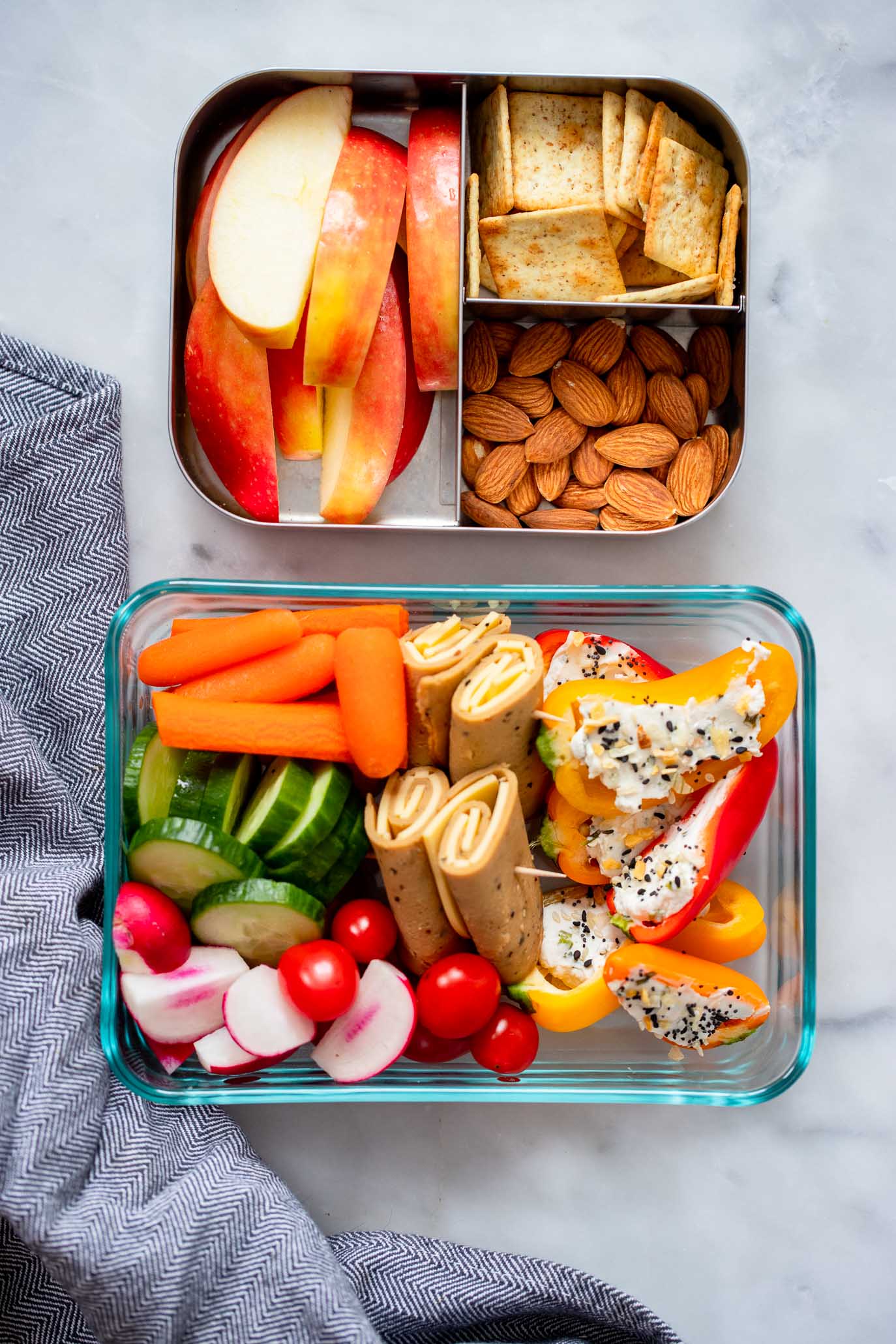 mini stuffed peppers in a bento box with carrots, deli slices, apples, and crackers. 