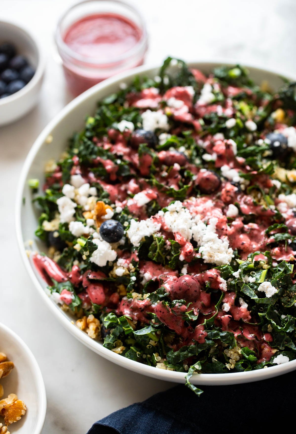 blueberry summer kale salad in white bowl with walnuts and vegan feta. 