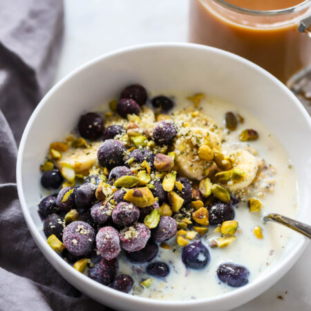 blueberry oatmeal topped with pistachios in a white bowl.