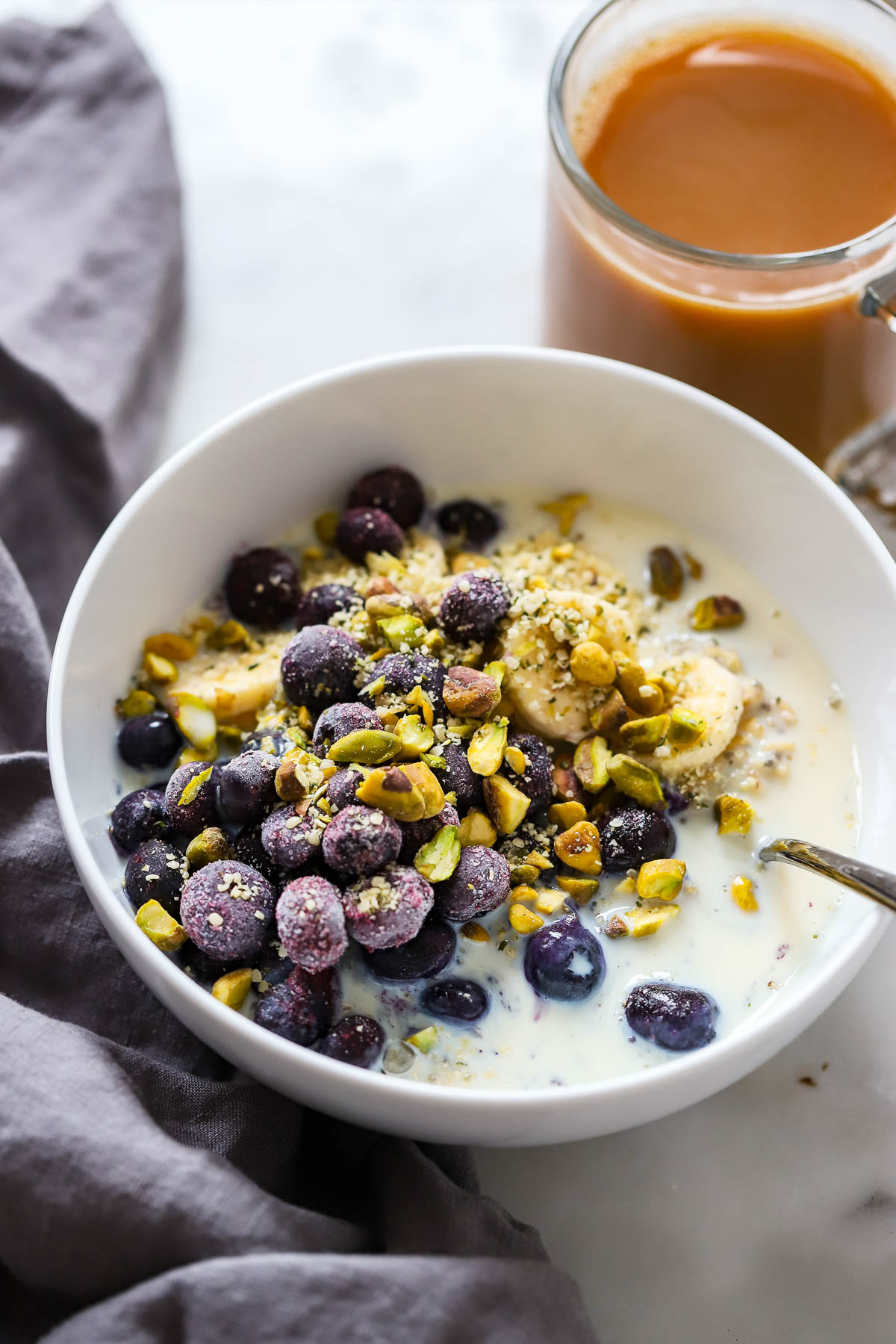 blueberry oatmeal topped with pistachios in a white bowl.