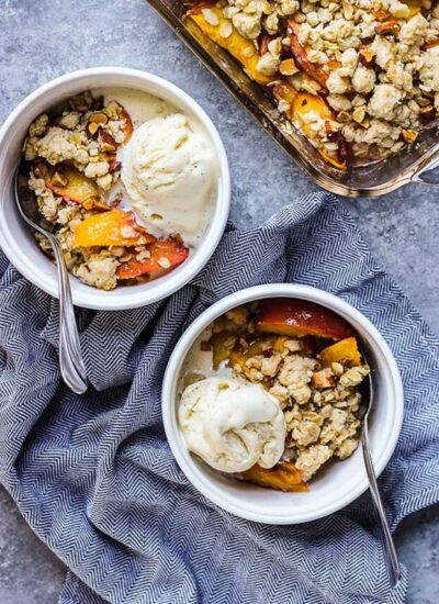peach crisp in 2 serving bowls with a spoon.
