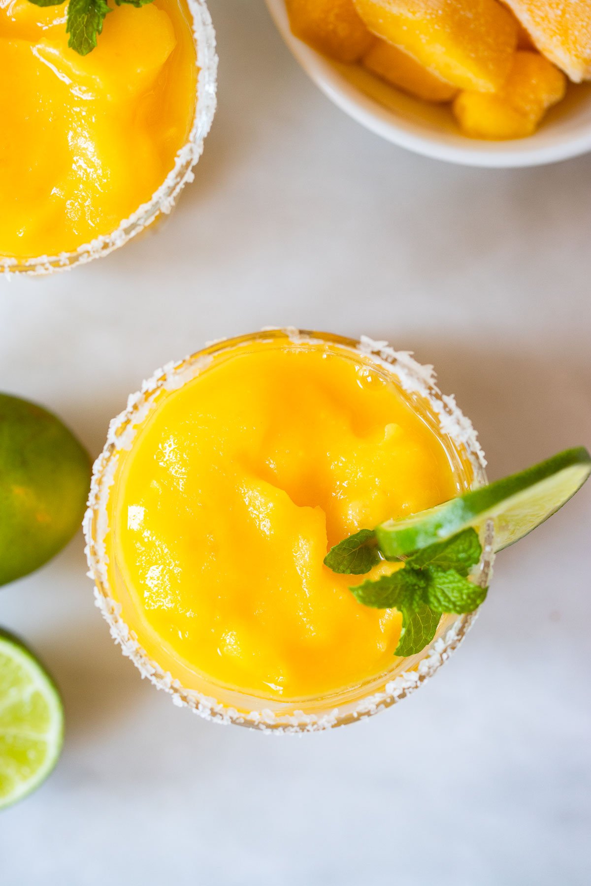 frozen mango margarita in salt rimmed glass with mint and lime.