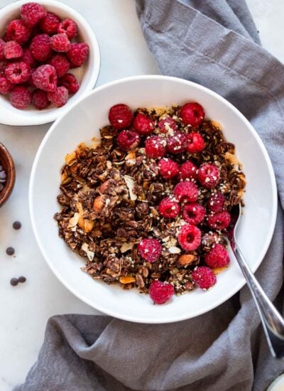 chocolate granola in white bowl with raspberries.