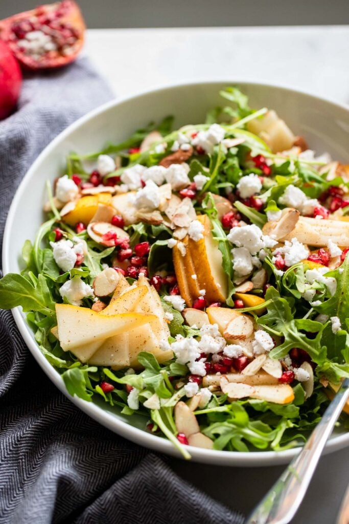 pear arugula salad with slivered almonds, vegan feta cheese, and pepper close up shot to see texture.