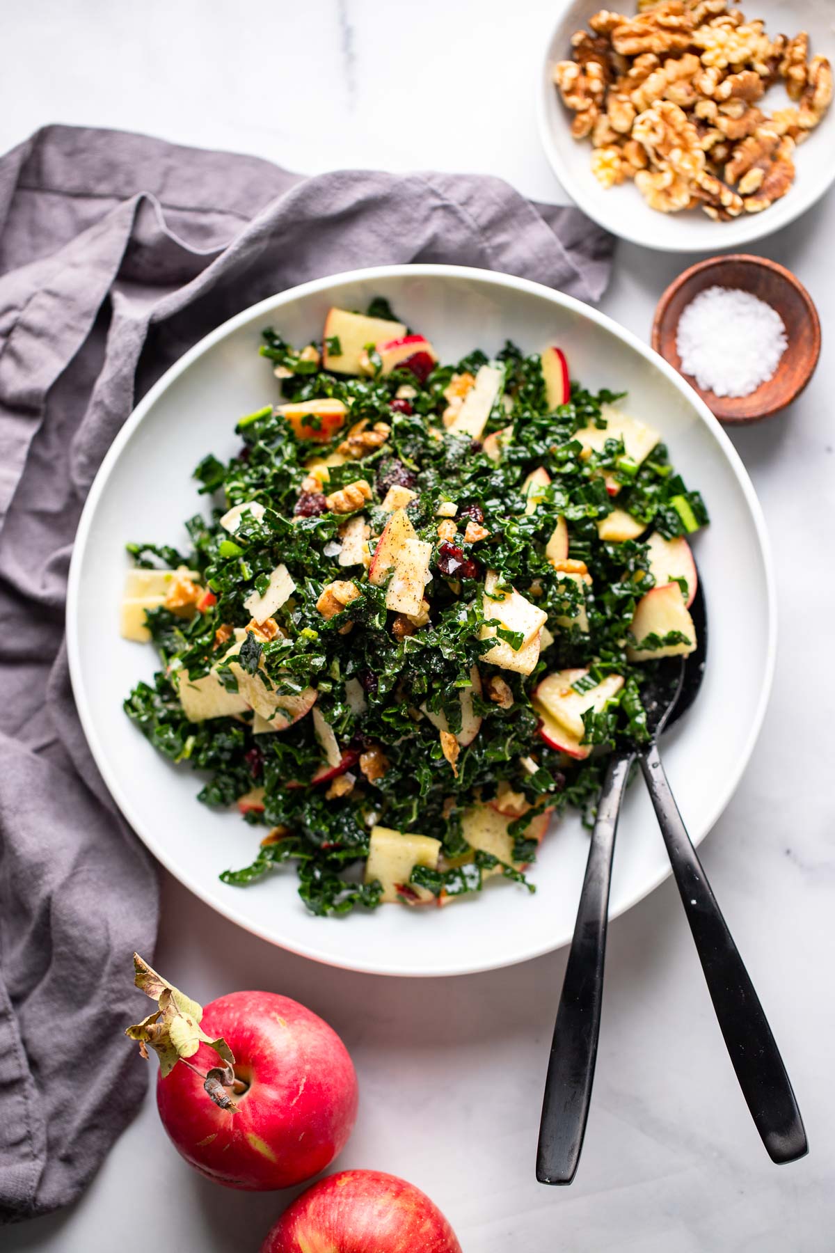 kale apple walnut salad in white bowl with spoons.
