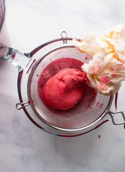 beet juice pulp wrapped in a cheesecloth sitting on a strainer. 