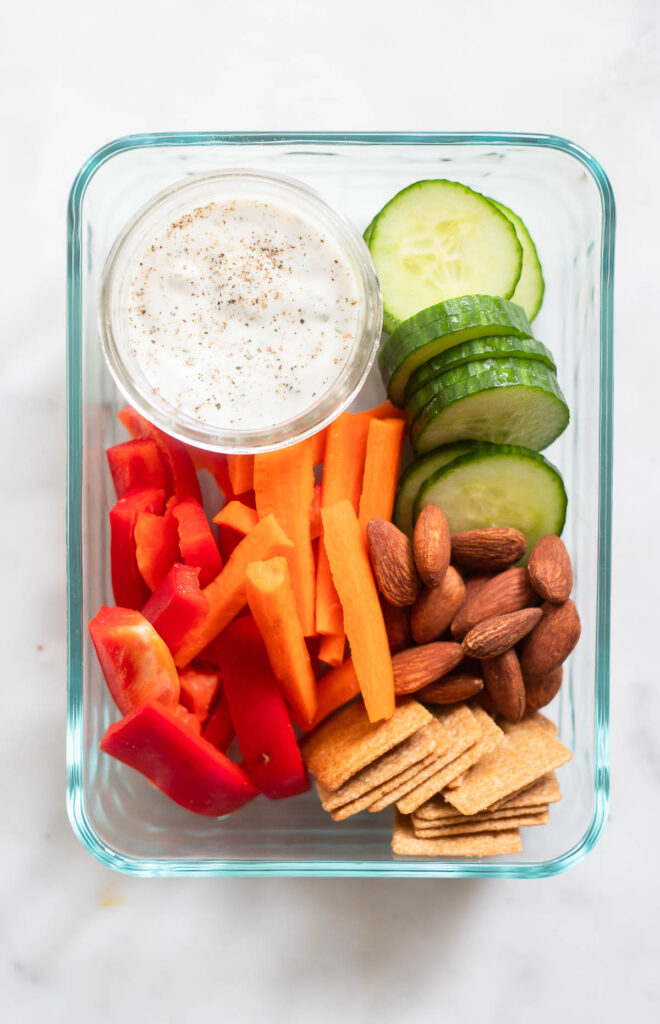 vegan ranch dressing in small cup in bento box with fresh vegetables. 