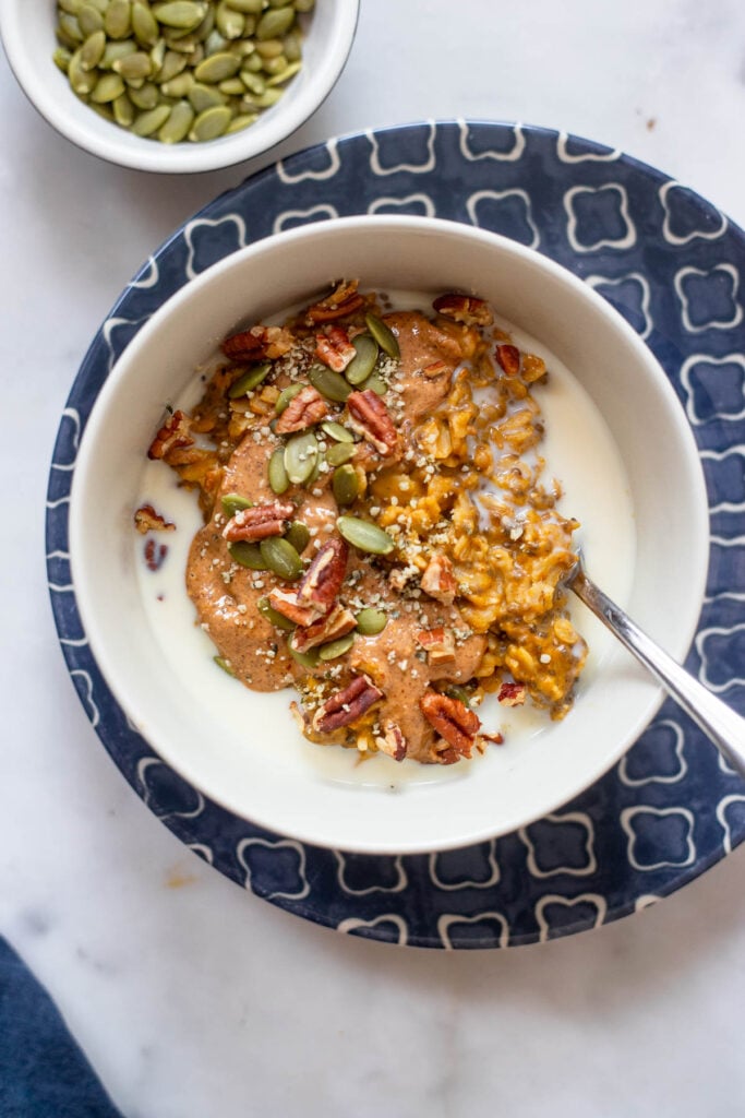 pumpkin oatmeal in bowl with almond butter, pumpkin seeds, and pecans.