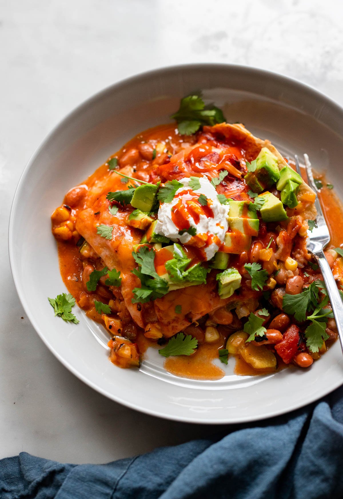 vegetarian enchilada slow cooker casserole in shallow bowl with avocado and sour cream.