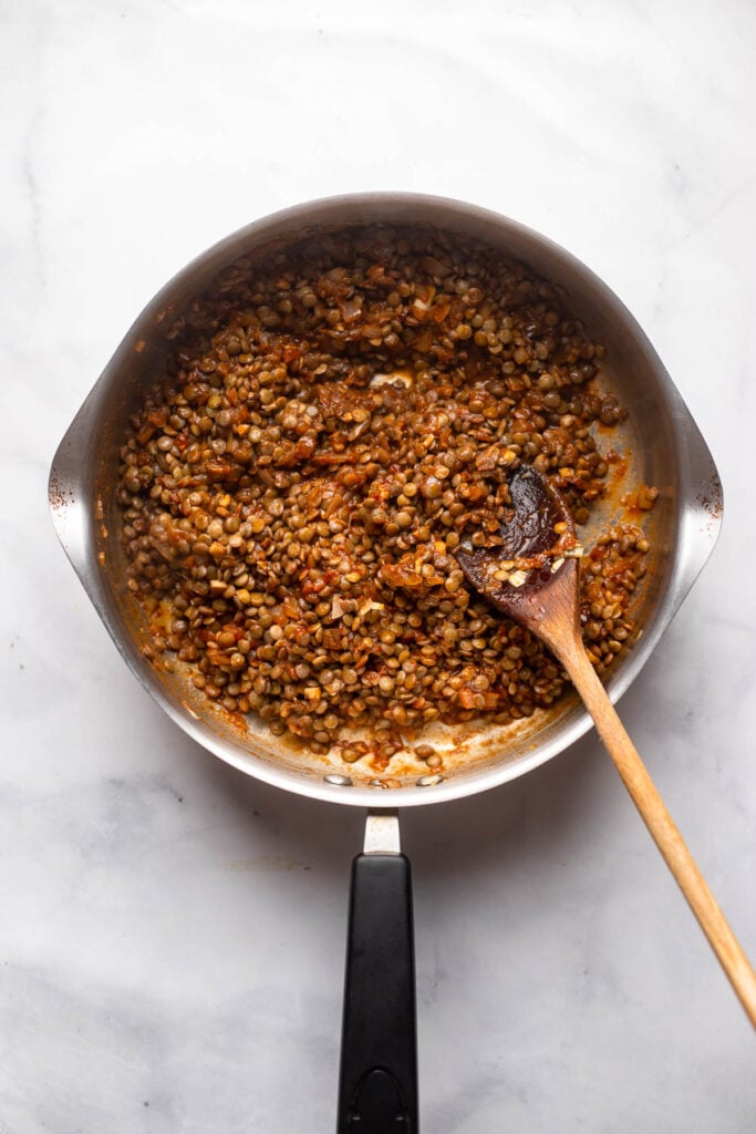 Cooked lentil filling in skillet with wooden spoon.