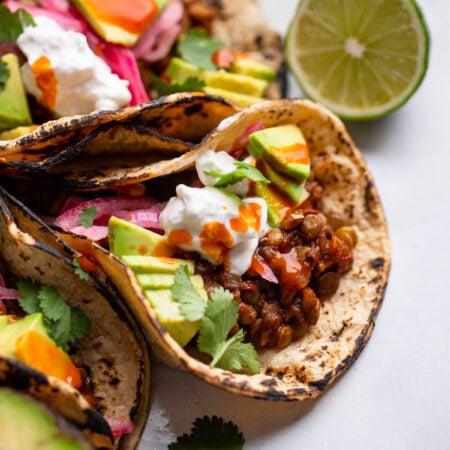 easy vegan lentil tacos garnished with avocado and hot sauce.