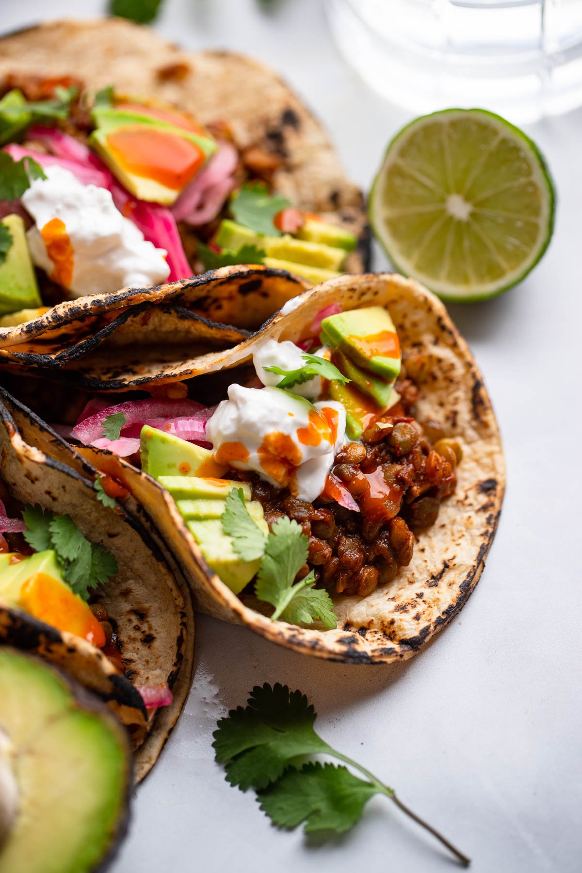 lentil tacos close up garnished with hot sauce, avocado, and sour cream.