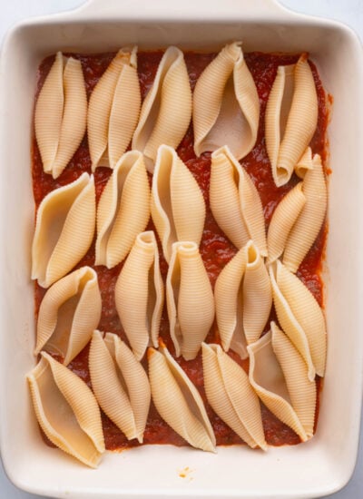 thin layer of sauce and pasta shells in baking dish.