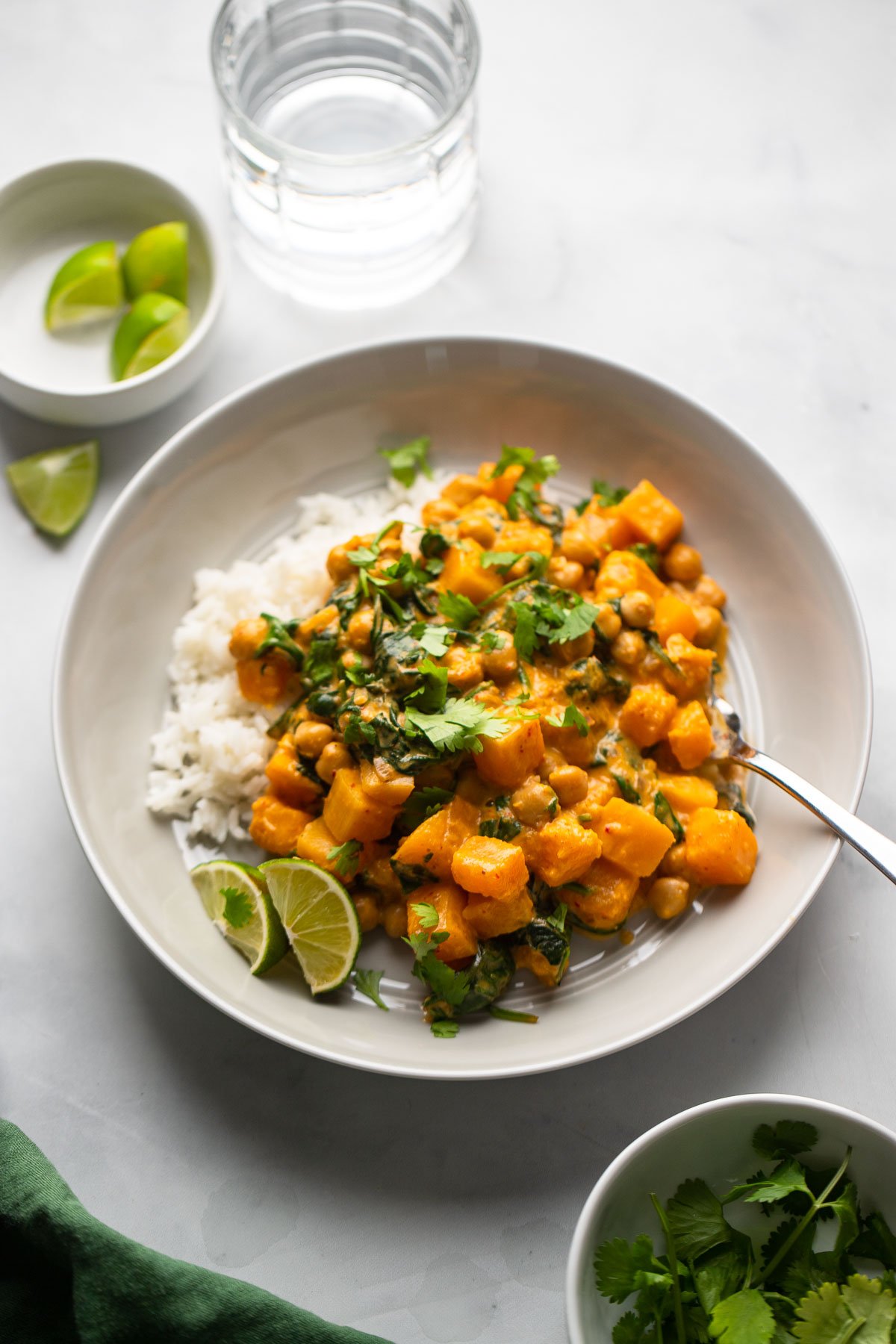 butternut squash and chickpea curry in low bowl garnished with cilantro and lime wedges.