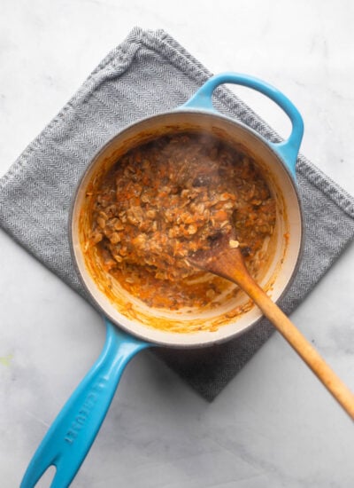 cooked carrot cake oatmeal in small saucepan with wooden spoon.