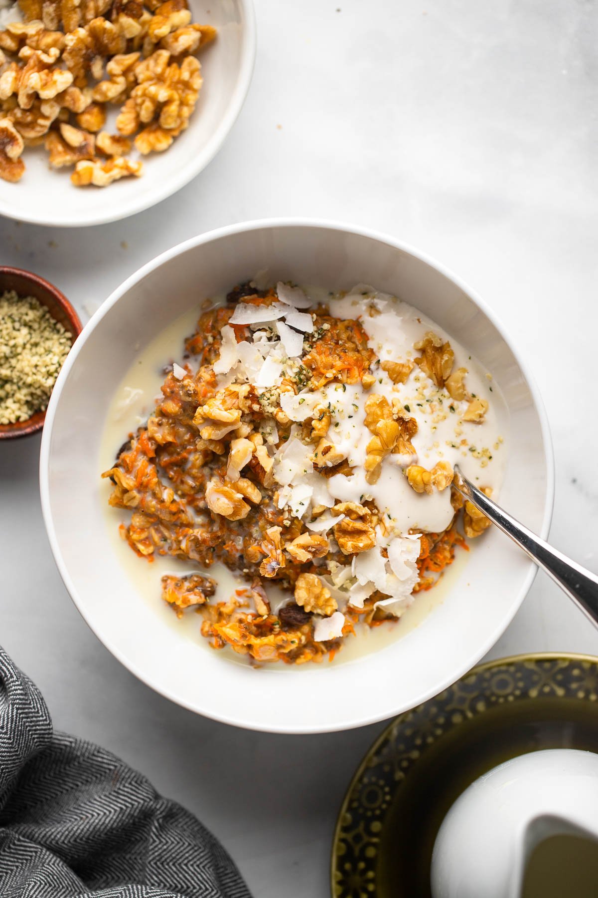 carrot cake oatmeal in white bowl garnished with chopped walnuts, coconut, and vanilla yogurt.