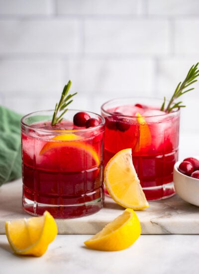 cranberry gin cocktail in two glasses garnished with fresh cranberries and lemon.