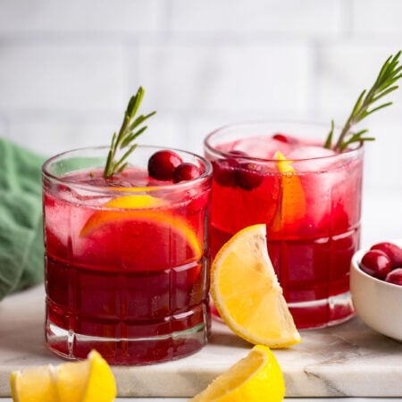 cranberry gin cocktail in two glasses garnished with fresh cranberries and lemon.