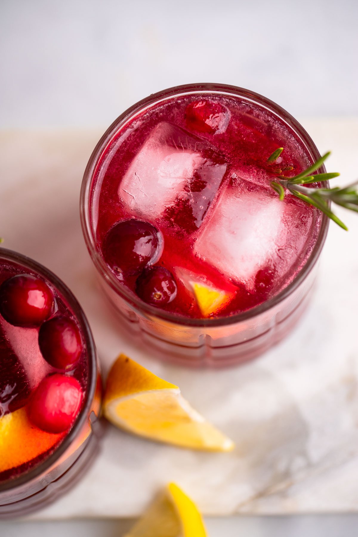 close up of cranberry gin cocktail with ice, cranberries, lemon, and rosemary.