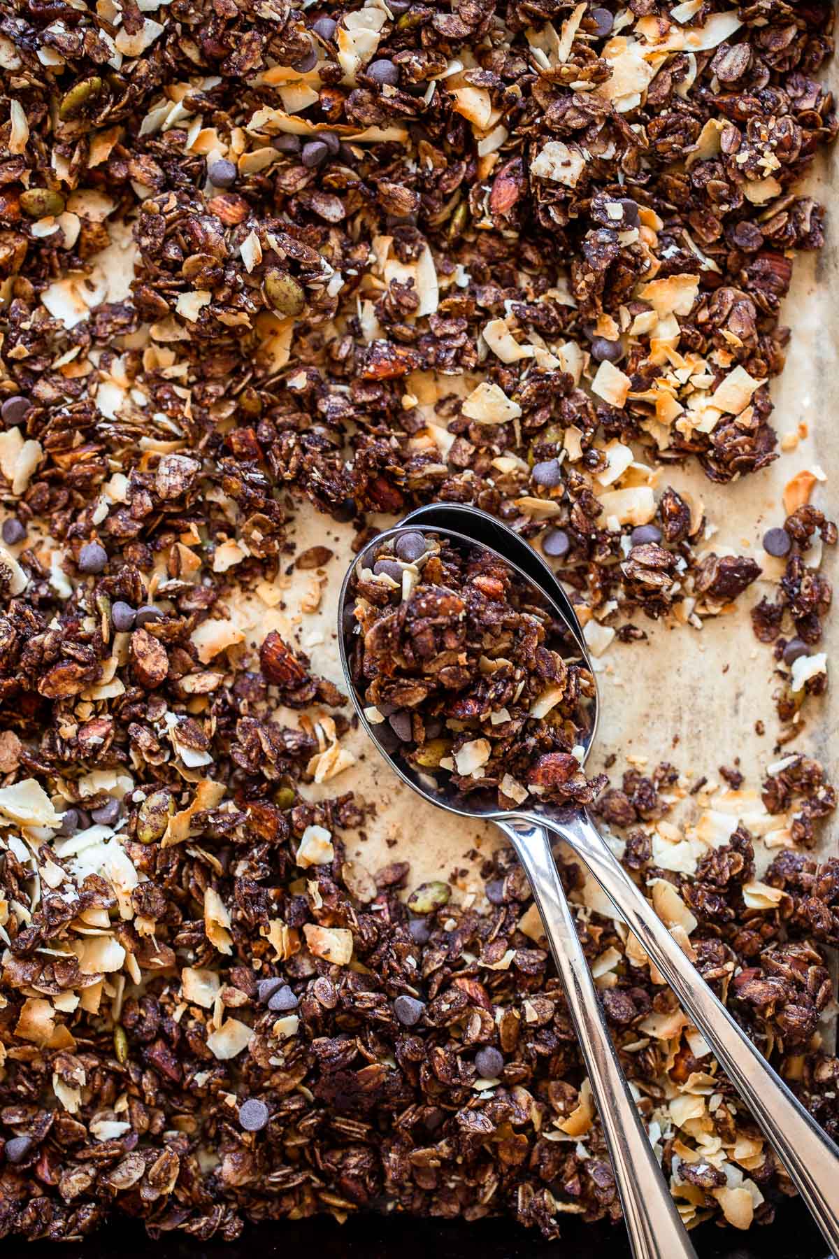 chocolate granola on baking sheet with spoons.