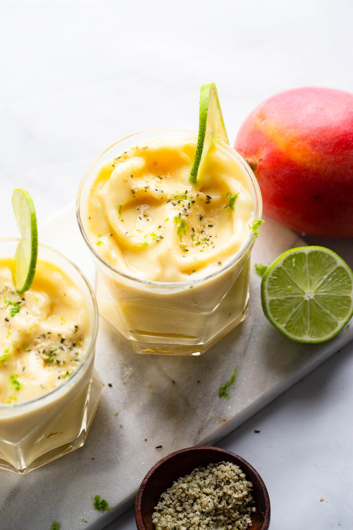 mango pineapple smoothie in glass with lime slice, lime zest, and hemp hearts.