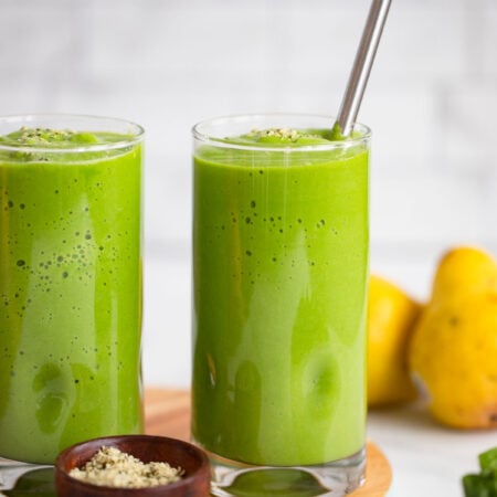 pear green smoothie in tall glass with metal straw.