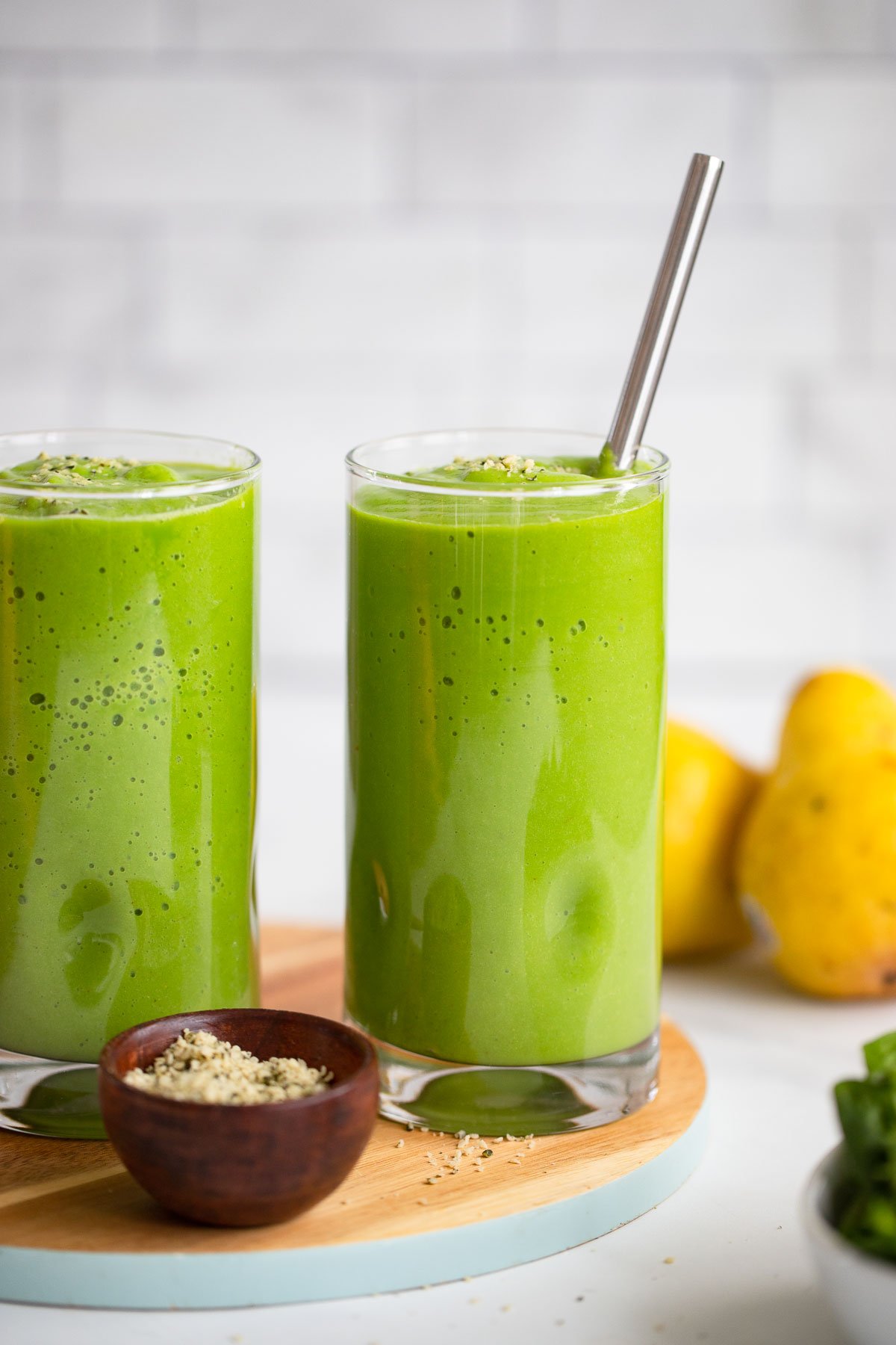 pear green smoothie in tall glass with metal straw.